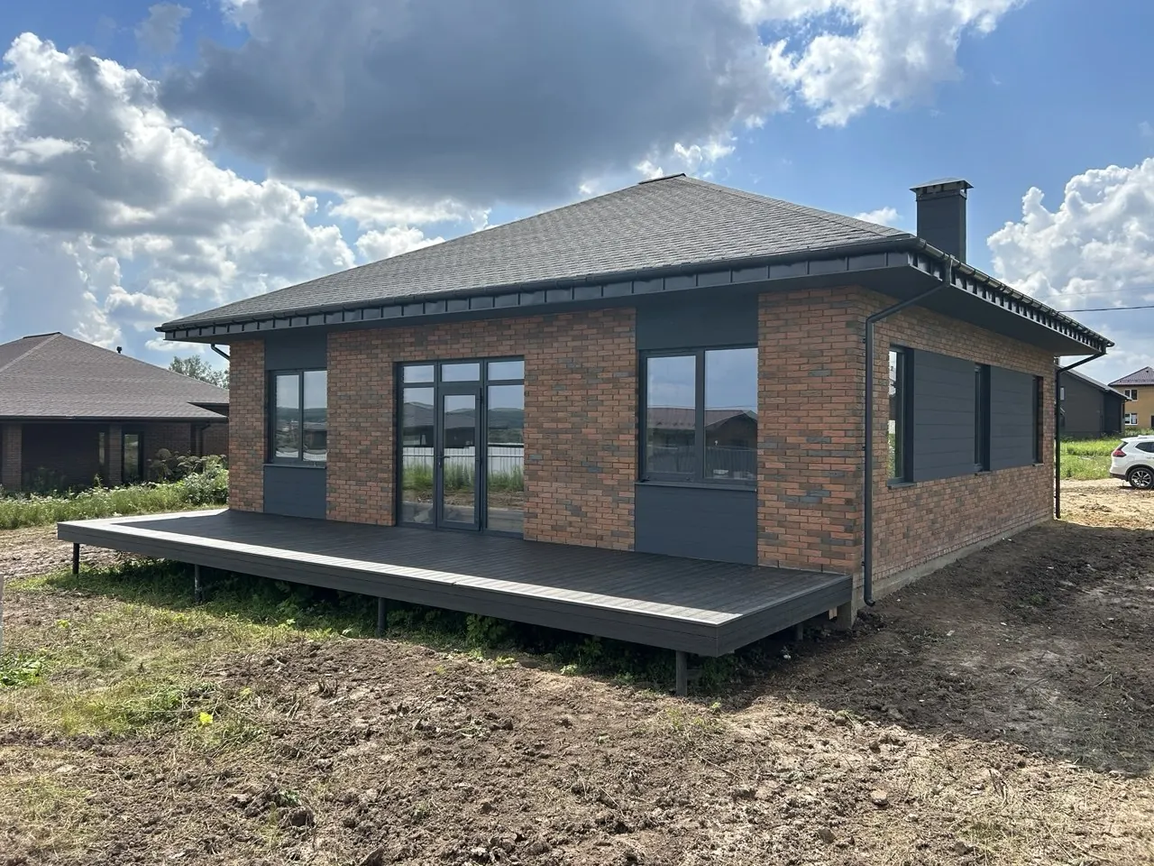 Одноэтажный дом из красного кирпича с графитовыми панелями и террасой