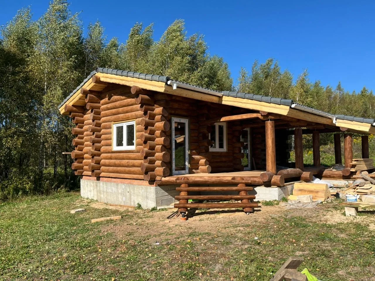 Рубленый дом из бревна с длинной открытой верандой на участке у леса